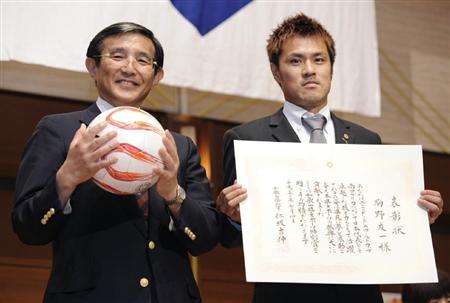 يوتشي كومانو ( يمين ) بعد حصوله على الجائزة من السيد ماساشي يوشينوبو ( يسار )