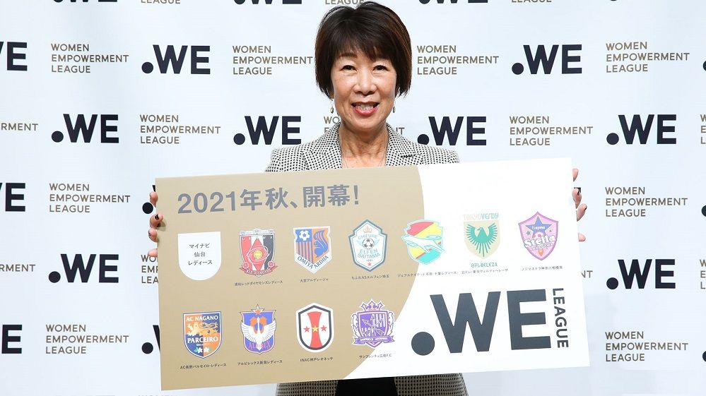 رئيسة الرابطة كيكوكو أوكاجيما مع شعار الدوري وأسماء الأندية المشاركة