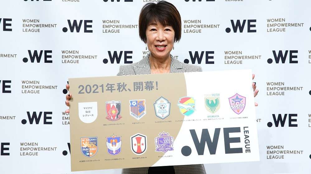 رئيسة الرابطة كيكوكو أوكاجيما مع شعار الدوري وأسماء الأندية المشاركة